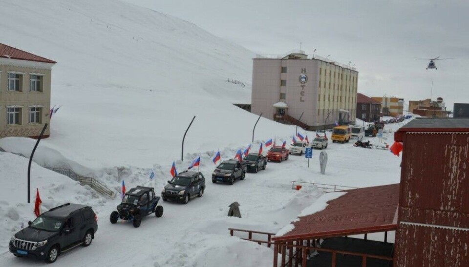 With the Consulate General’s diplomatic car in front and a low-flying MI8 helicopter above, the military-style Russian May 9 parade continued along the snow-covered road in Barentsburg. Photo courtesy of Arktikugol