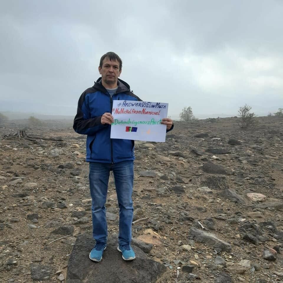 Andrei Danilov stands in the ecological disaster zone near Monchegorsk, holding a poster urging Elon Musk to answer the call from indigenous peoples of the Russian north not to by metals from Nornickel. Photo: Private