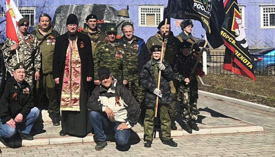 Archpriest Aleksandr Koptev maintains close ties with the Armed Forces. In May 2022, he teamed up with this group of soldiers at the Onega memorial, laying flowers to honor those who died in military conflicts. Like the others, he wears the Ribbon of Saint George, a symbol that after Russia’s war on Ukraine in 2014 has become more controversial, due to its association with the separatist regions, militarism, and Russian nationalism. The flags to the right are the symbols of the mobile infantry brigade and the marine infantry special forces. Photo: Church of Plesetsk and Kargopol