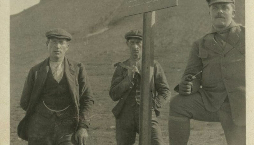 Three men stand around a sign claiming mining rights for Store Norske Spitsbergen Kulkompani. Nansen did not consider coal mining on Spitsbergen a sensible endeavour, and disliked the effect industry had on the Arctic landscape.
