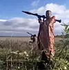 Man in Orthodox vestments aiming a grenade launcher in an open field